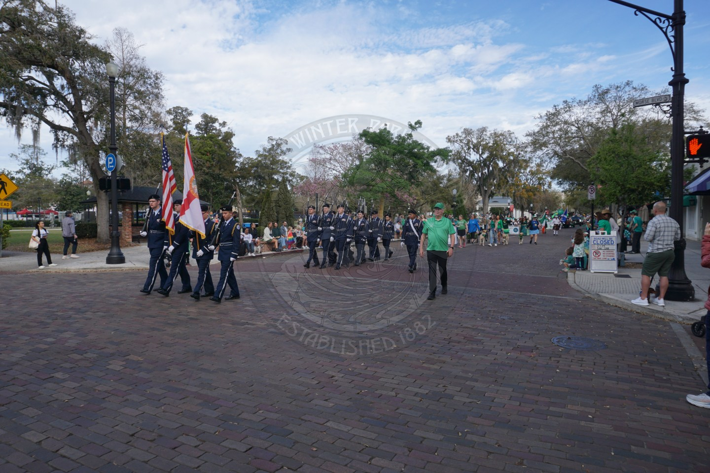 uniformed group of people marching down a brick street.