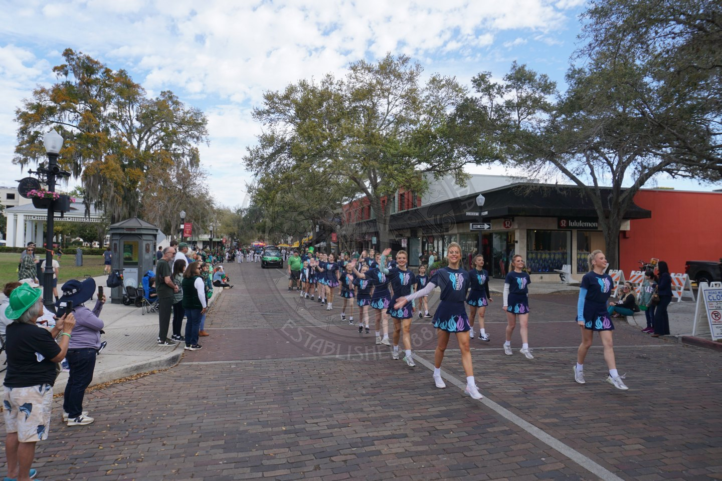 group of young cheerleaders marching down a brick street dancing.