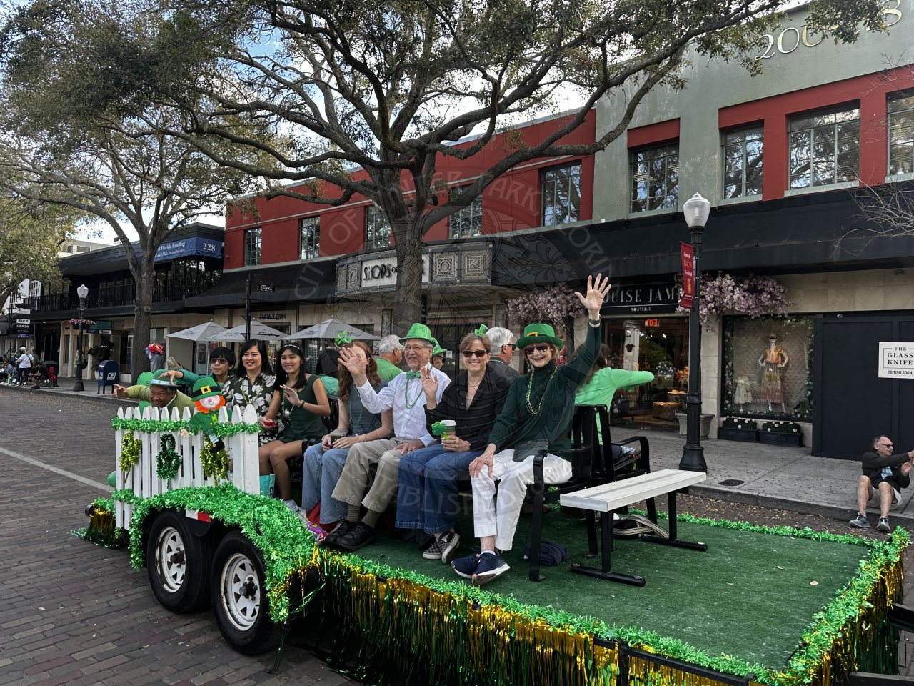 group of comissioners sitting on benches on a trailer riding down a brick street.