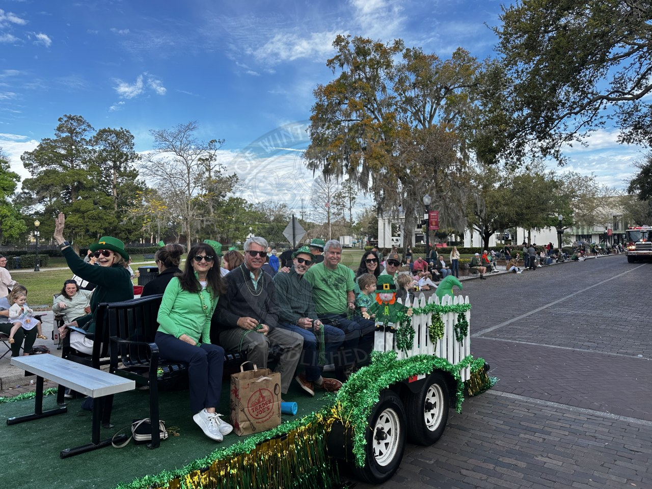 group of comissioners sitting on benches on a trailer riding down a brick street.