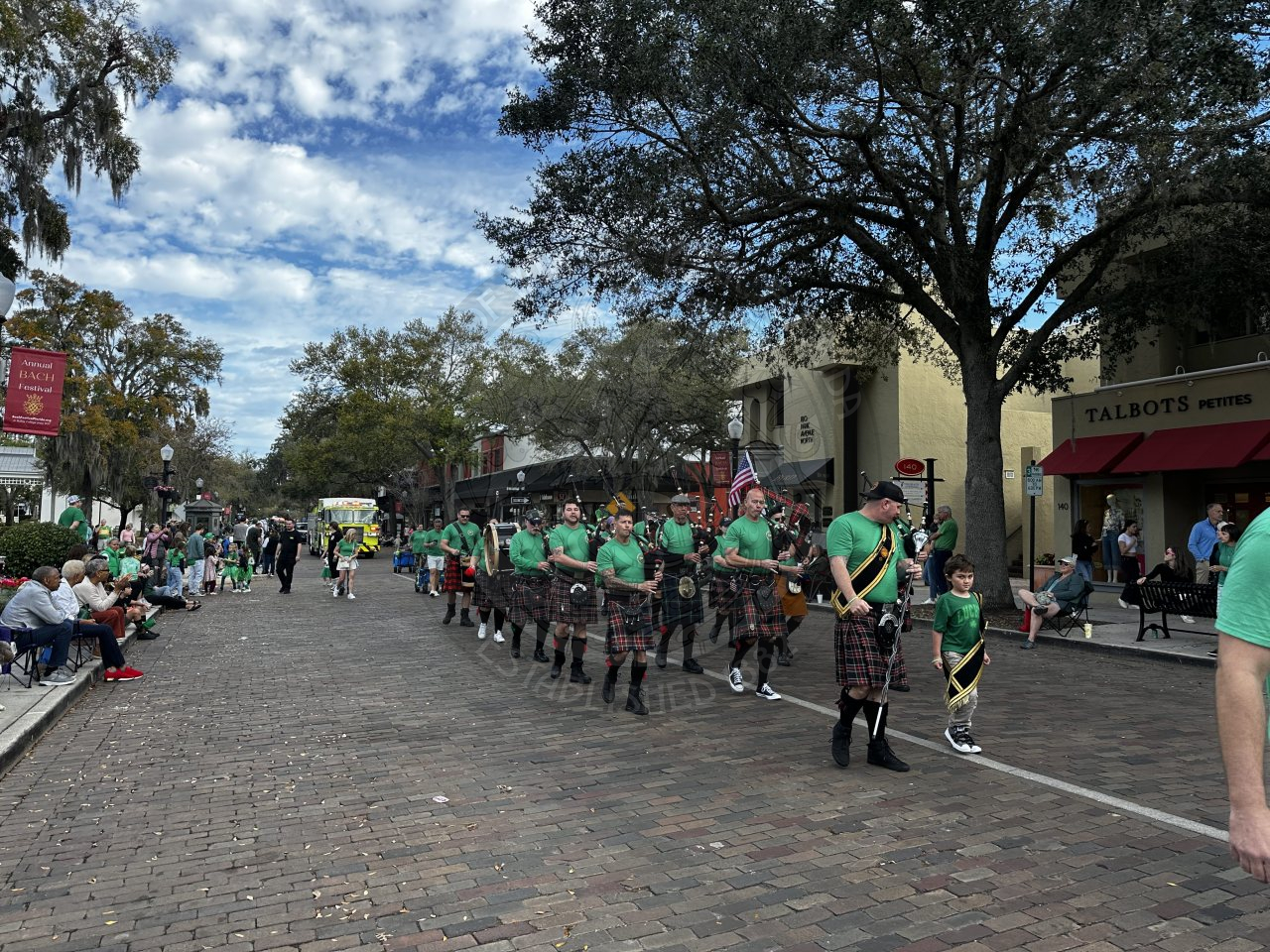 a group of men wearing kilts and playing banjos and the drums walking on a brick street.