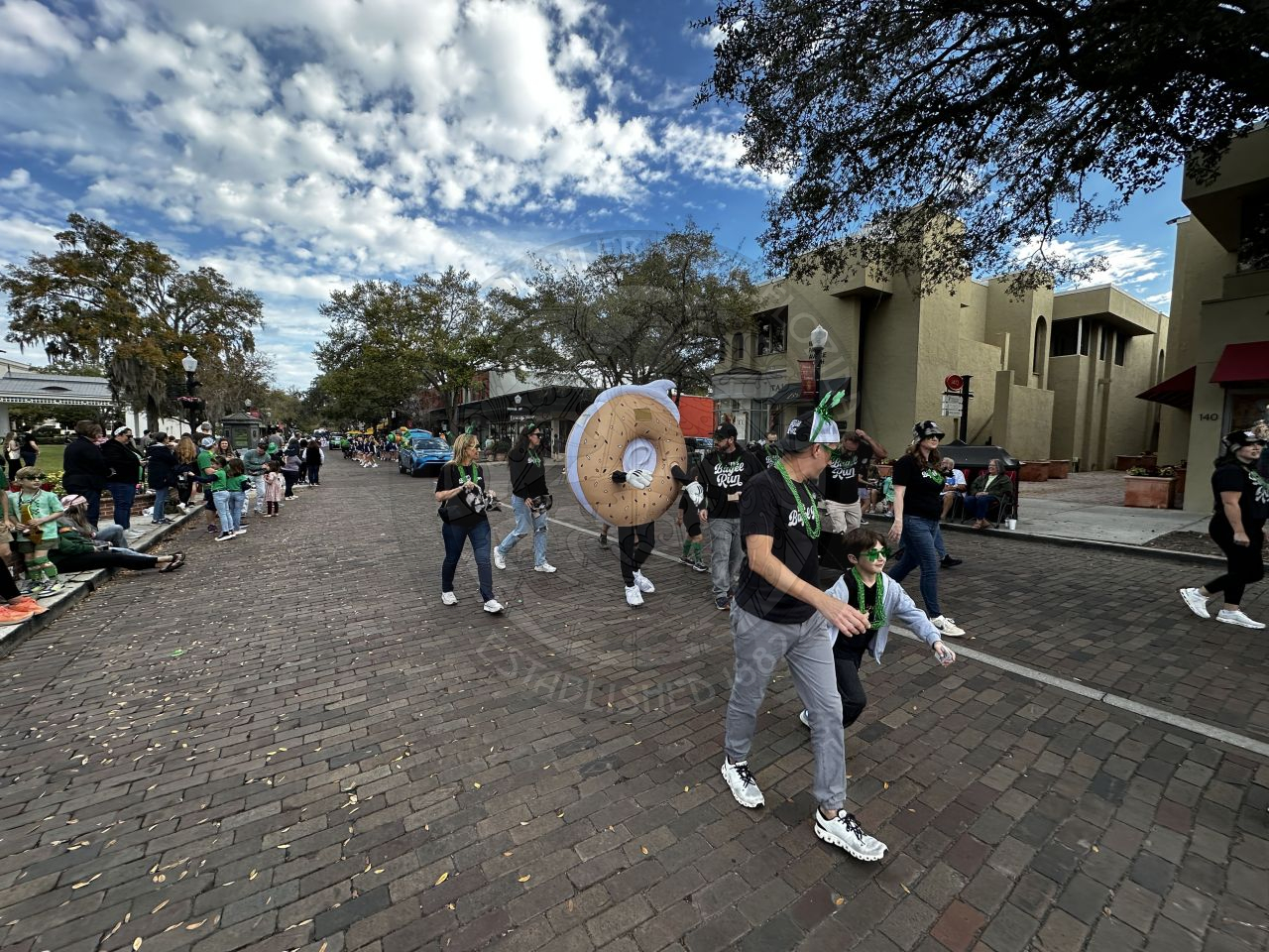 people walking down a brick street with someone in the middle in a bagel blowup