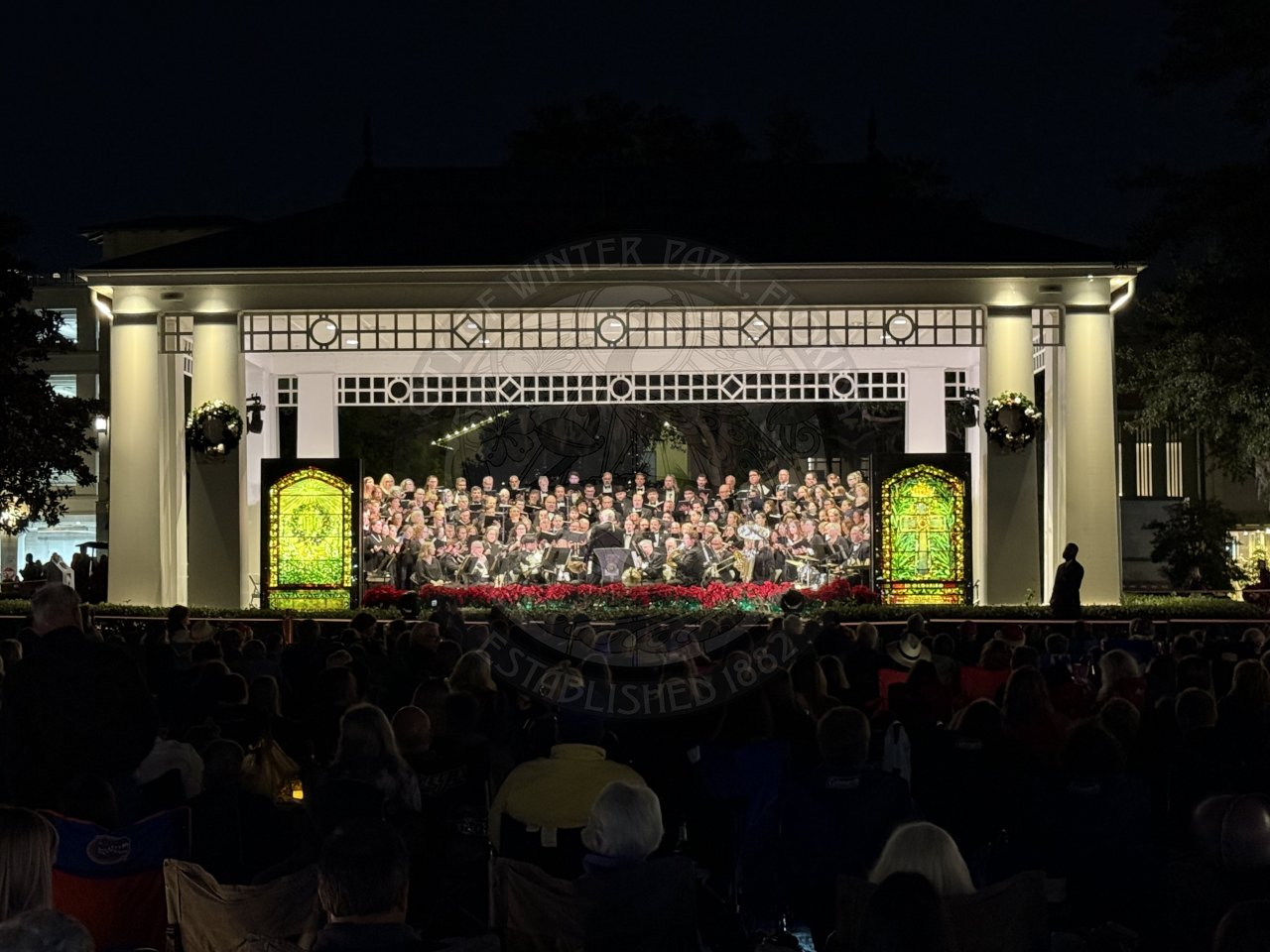 A symphony orchestra sitting on stage with two tiffany mirrors on the side of the stage