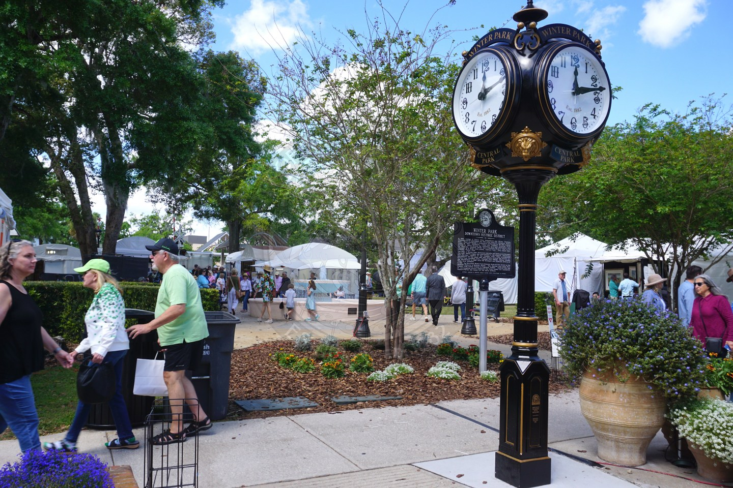 Historic clock with tents and people looking at art in the background