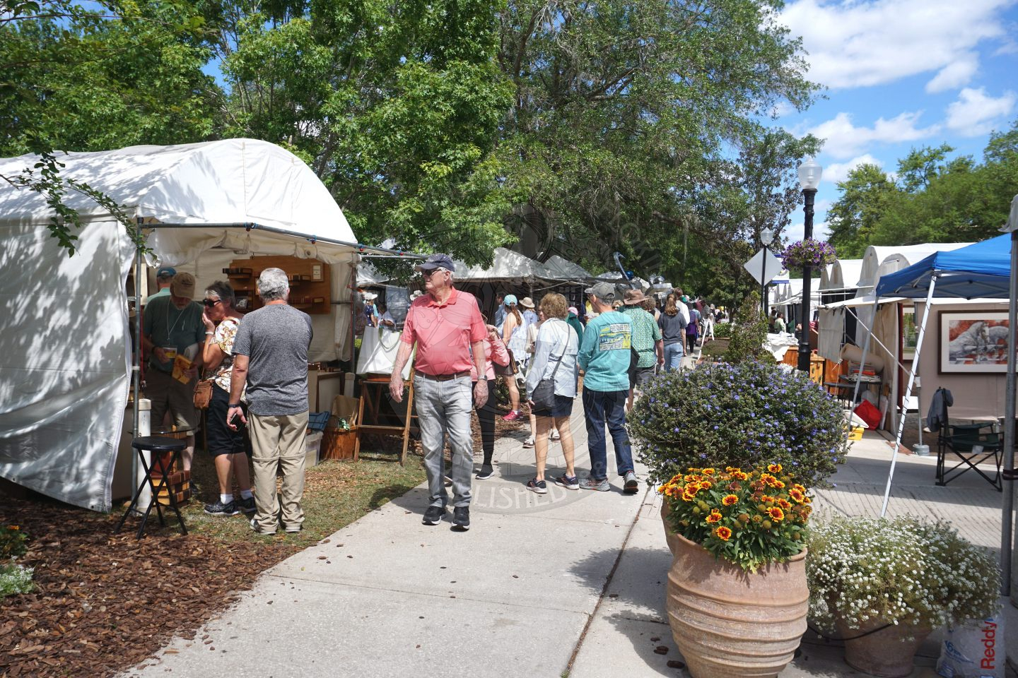 people walking on the sidewalk looking at tents with art in them