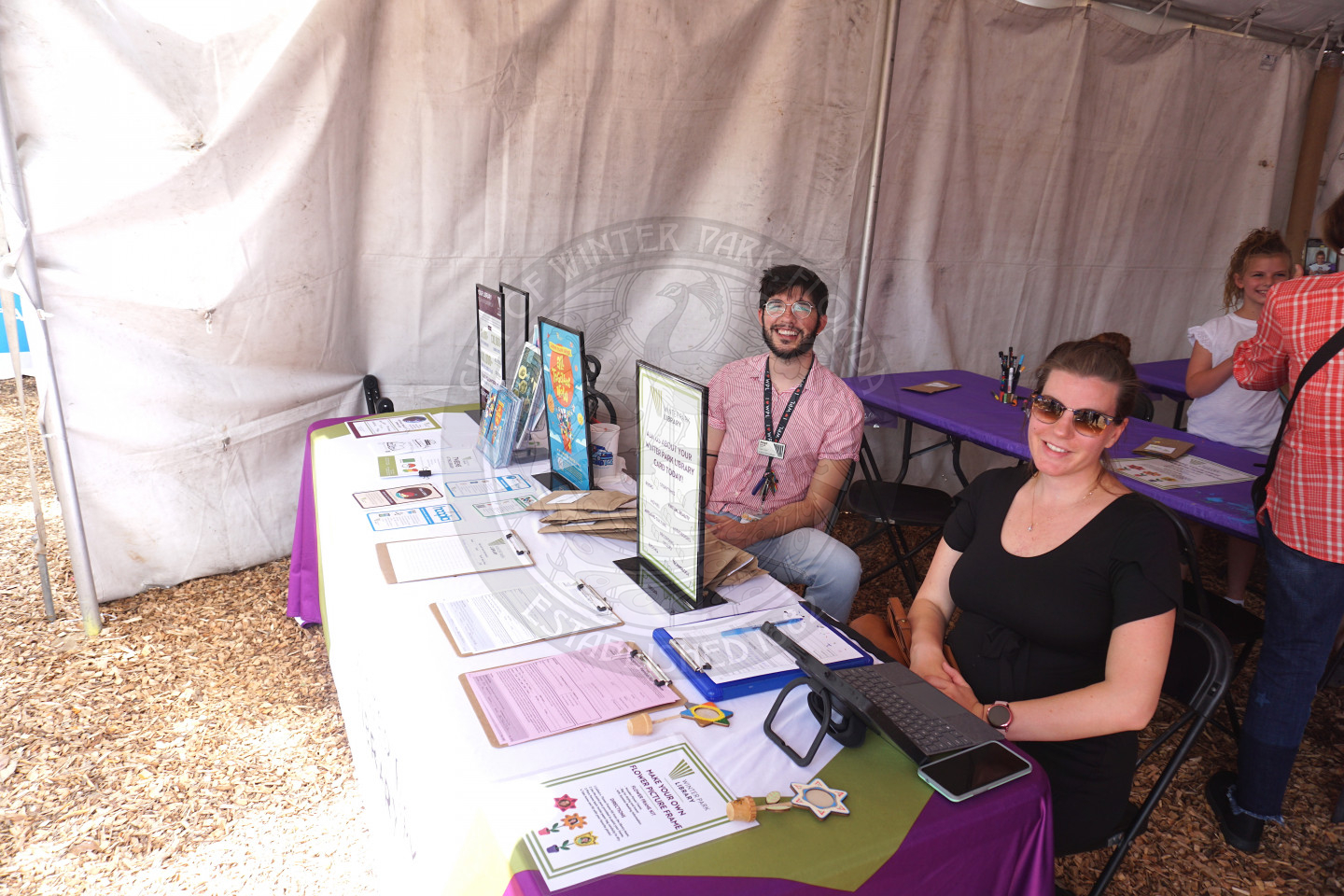 a photo of a man and woman sitting in chairs sitting behind a table advertising the Winter Park Library