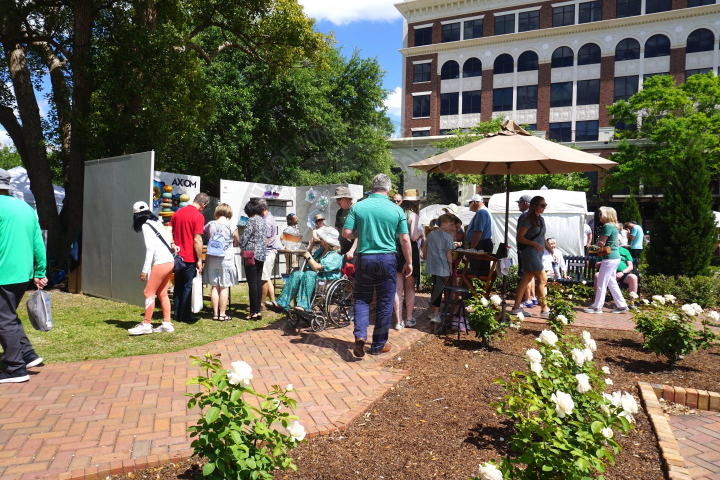 part of the rose garden and poeple walking on sidwalk path looking at tents filled with art