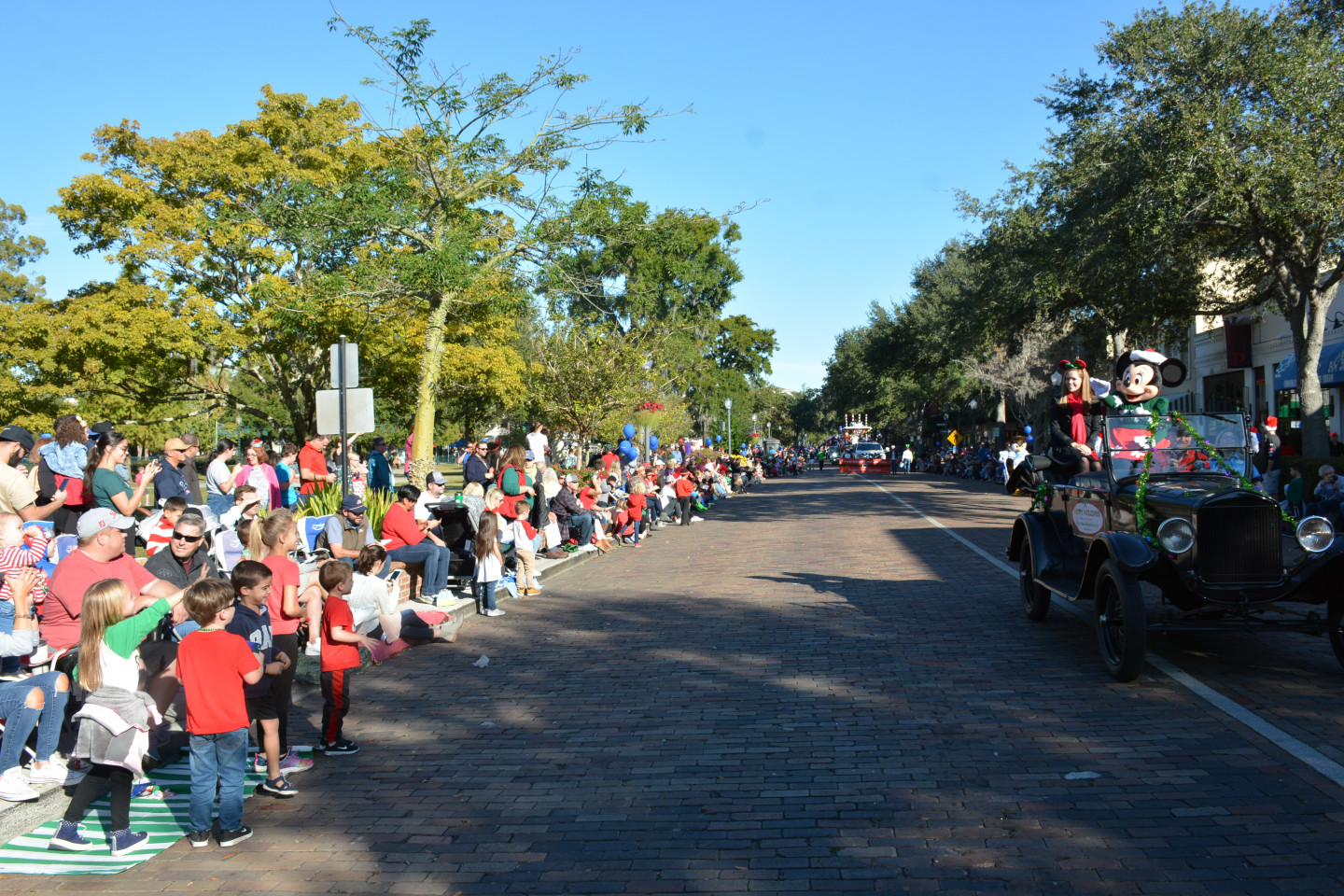 Minnie Mouse waving from a car to crowd of kids sitting on the sidewalk
