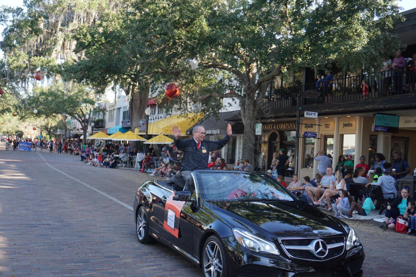 Man sitting in the back of a Mercedes with the top down waving to the crowd