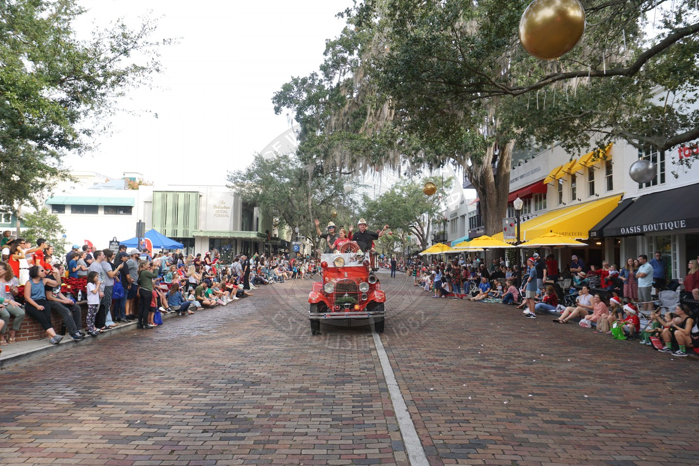 a scenic view of Park Avenue with an antique fire truck driving down the road with Santa and Mrs. Clause standing the back.