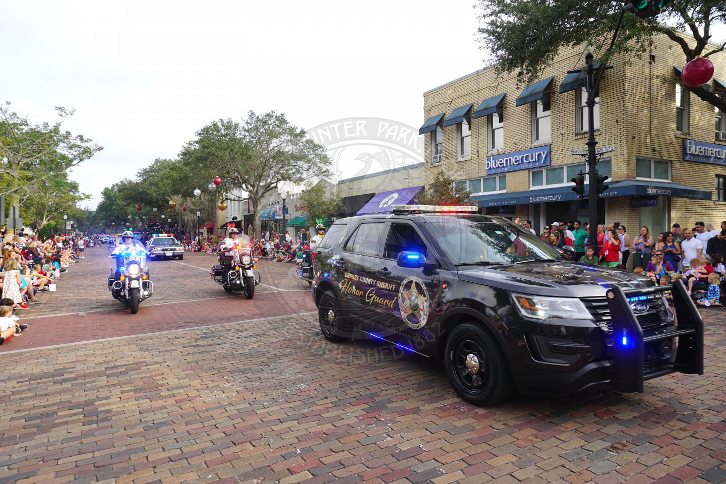 Orange County Sherriff Honor Guard vehicle with the lights on driving by with three sherriff motocrycles behind the car.
