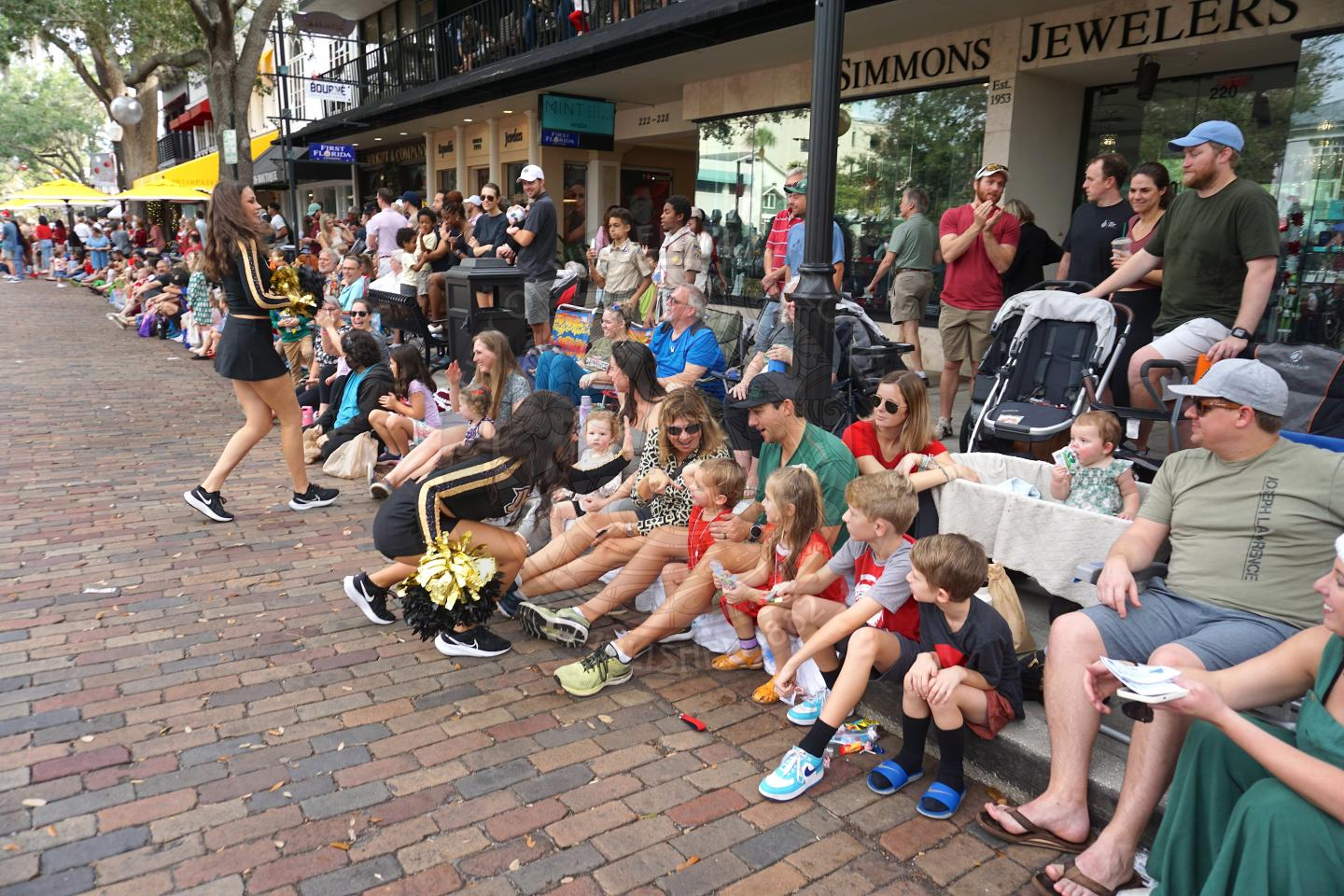 two UCF cheerleaders bending down to give little kids high fives that are sitting on the sidewalk of Park Avenue.