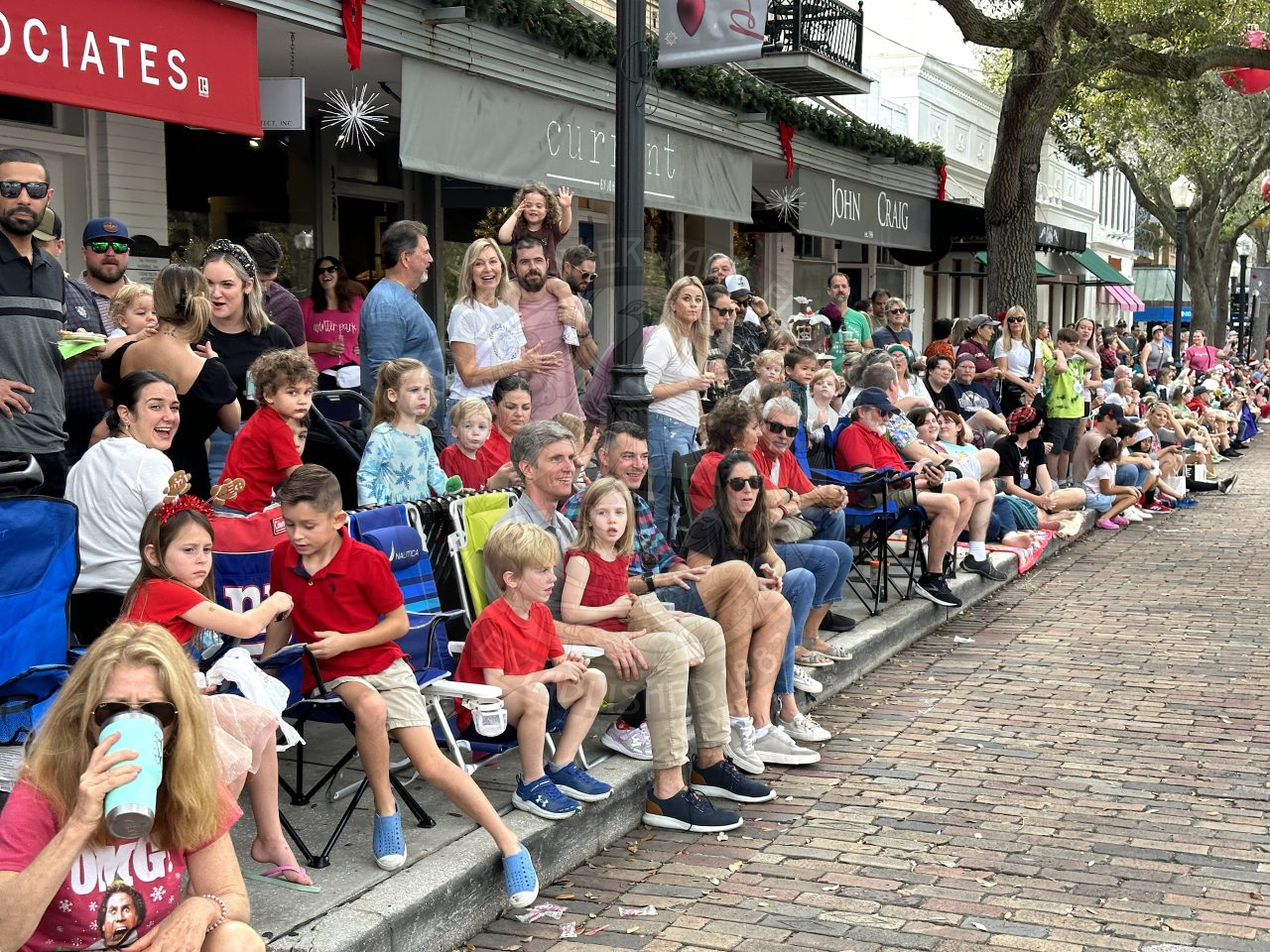 People sitting and standing on the sidewalks of Park Avenue to watch all the floats ride by  for the Christmas Parade