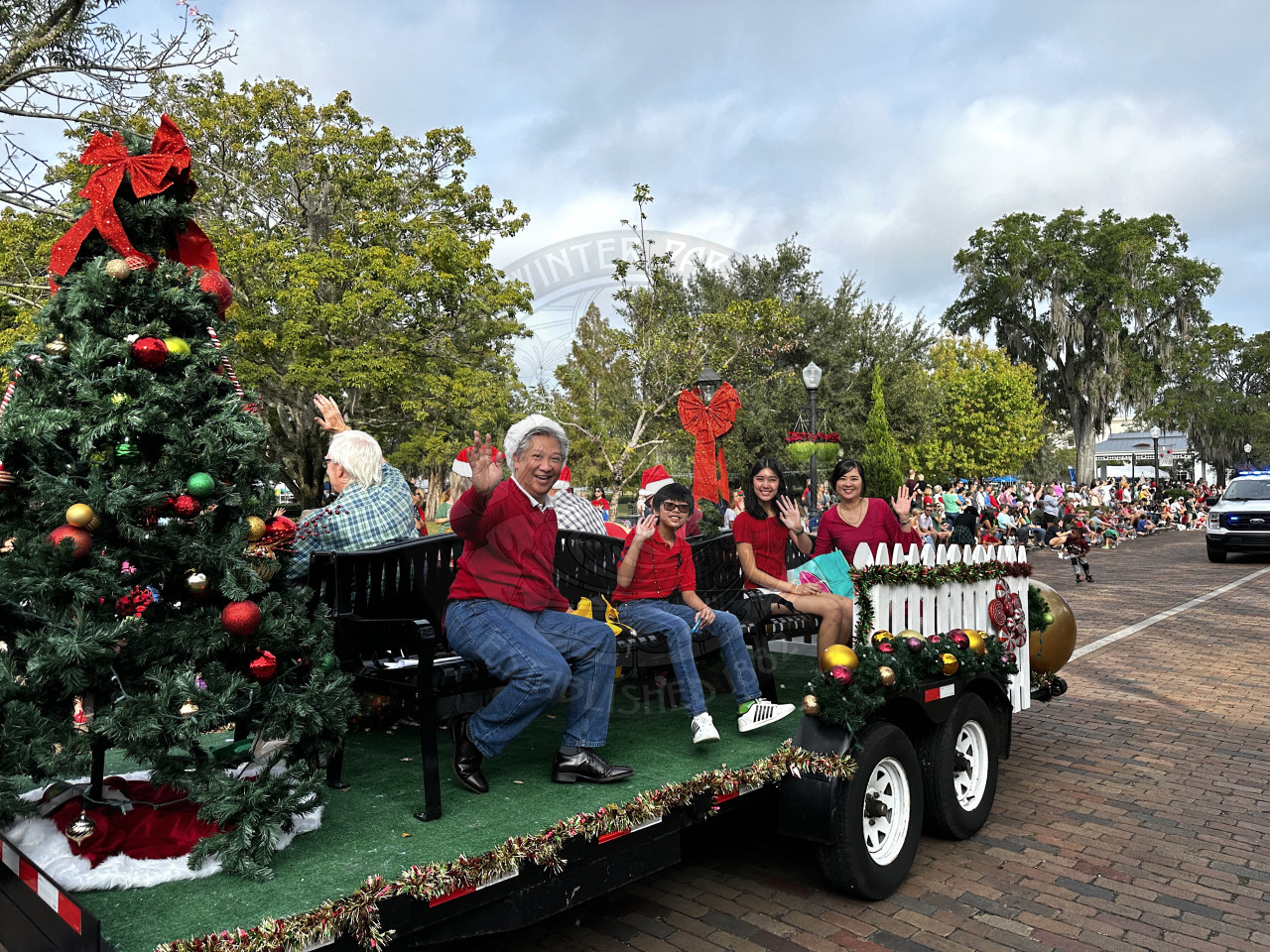 Commisioner Cruzada and his family sitting on benches that are on a trailer for a christmas parade. They are all smiling and waving as they ride on Park Avenue.