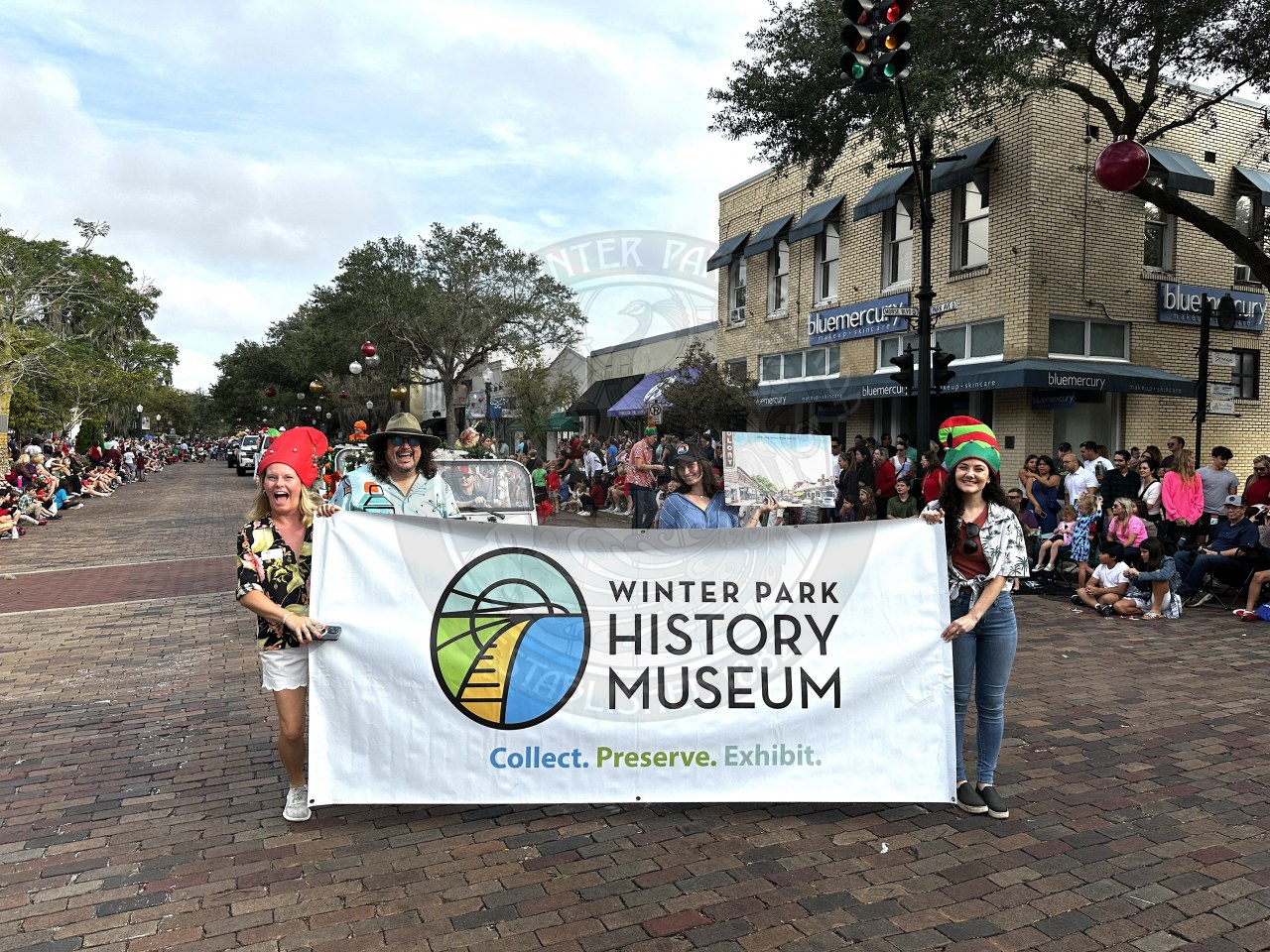Two women walking on Park Avenue smiling and are on opposite sides of a big banner that says Winter Park history Museum.