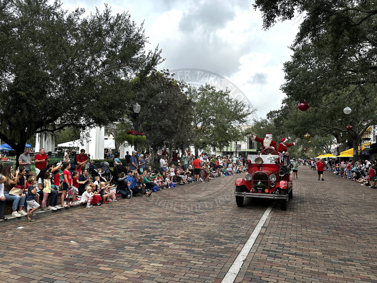 Santa and mrs. claus standing in the back of an antique fire engine that is driving on Park Avenue for the Christmas Parade.