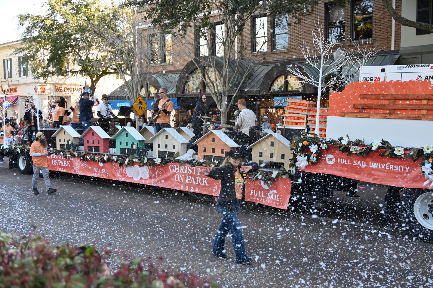 A trailer with a full band on it playing music and fake snow blowing out onto the street.