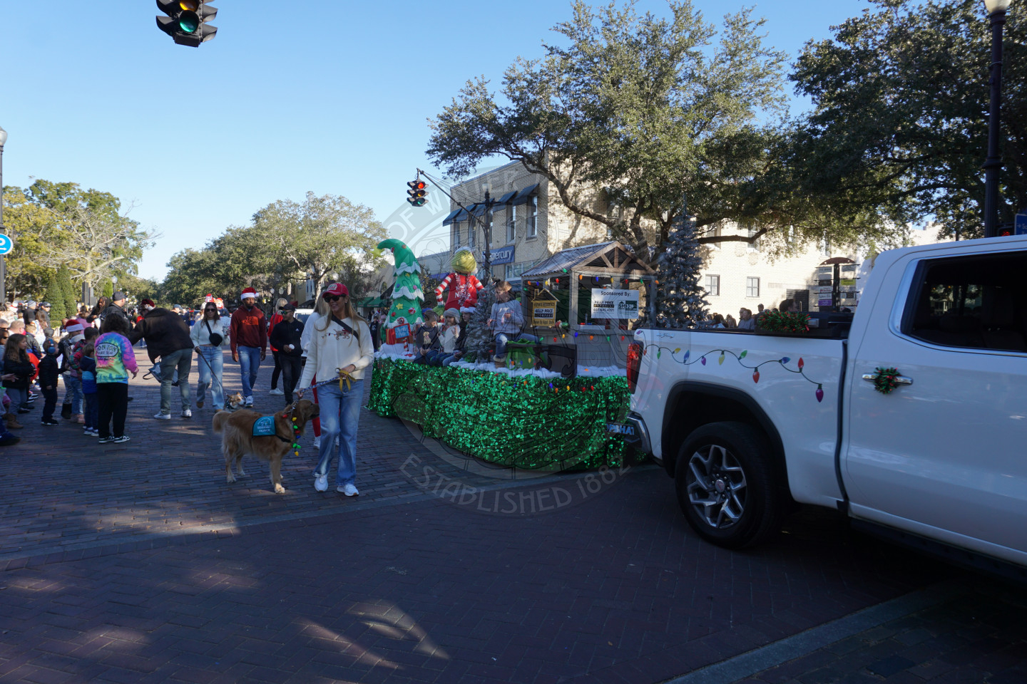 a truck with a trailer behind it and people walking next to it dressed in Christmas gear.