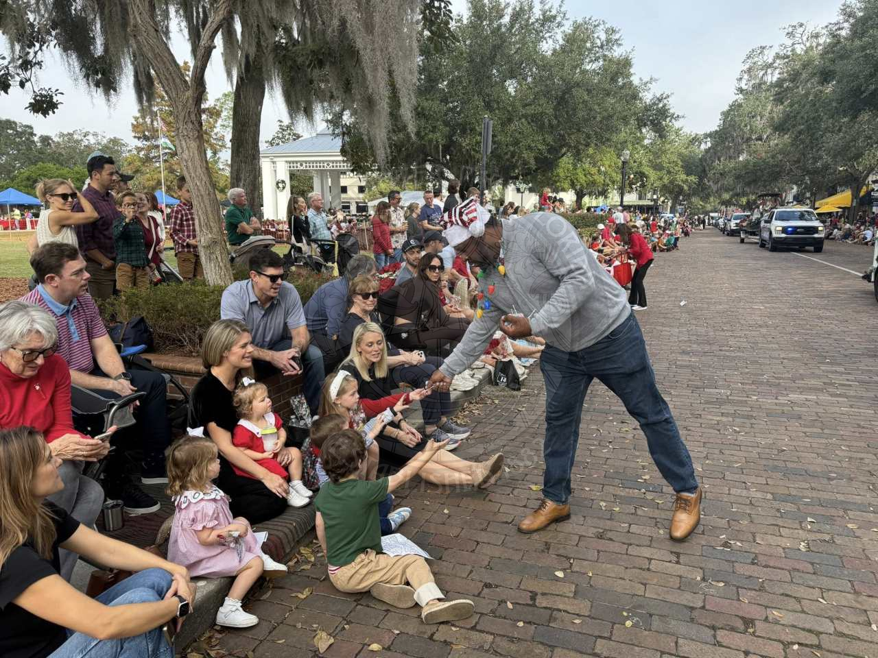a man passing out candy to children sitting on the sidewalk watching parade floats.