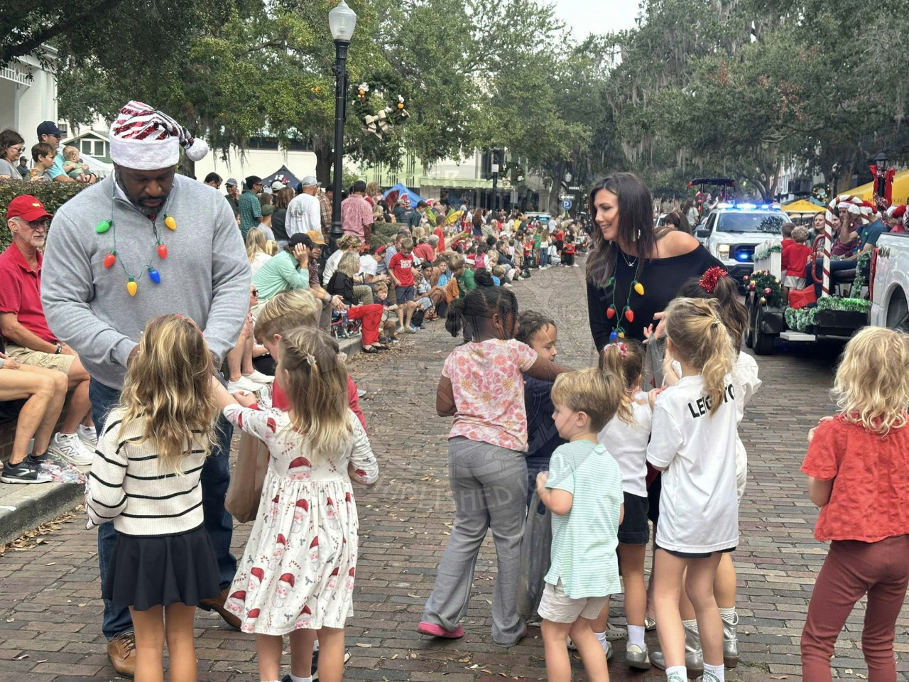 a man and woman handing out candy with a bunch of children surrounding them try to grab the candy.
