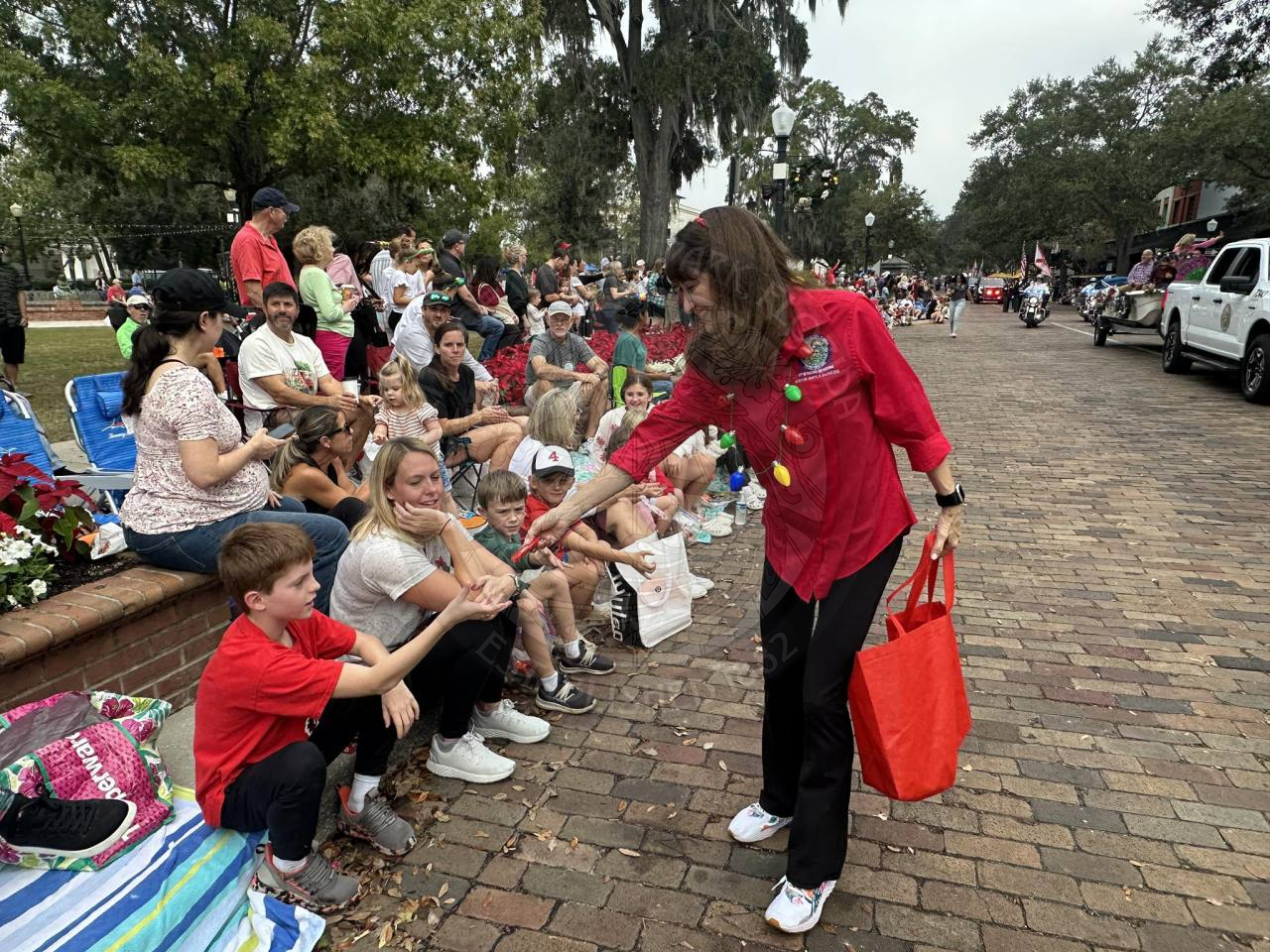 a woman walking along brick road passing out candy to the people watching the parade.