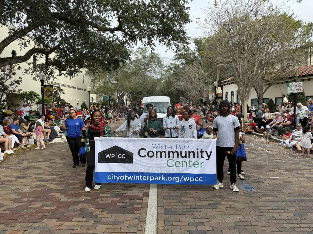 a group of people standing together in a gorup walking in a parade with a sign saying "Winter Park Community Center"