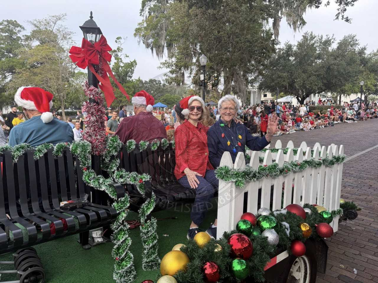 a man and a woman sitting on a bench riding around on the parade route.