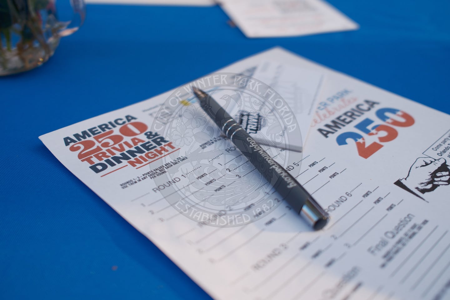 Close-up of an America 250 Trivia Night answer sheet and pen on a blue tablecloth.