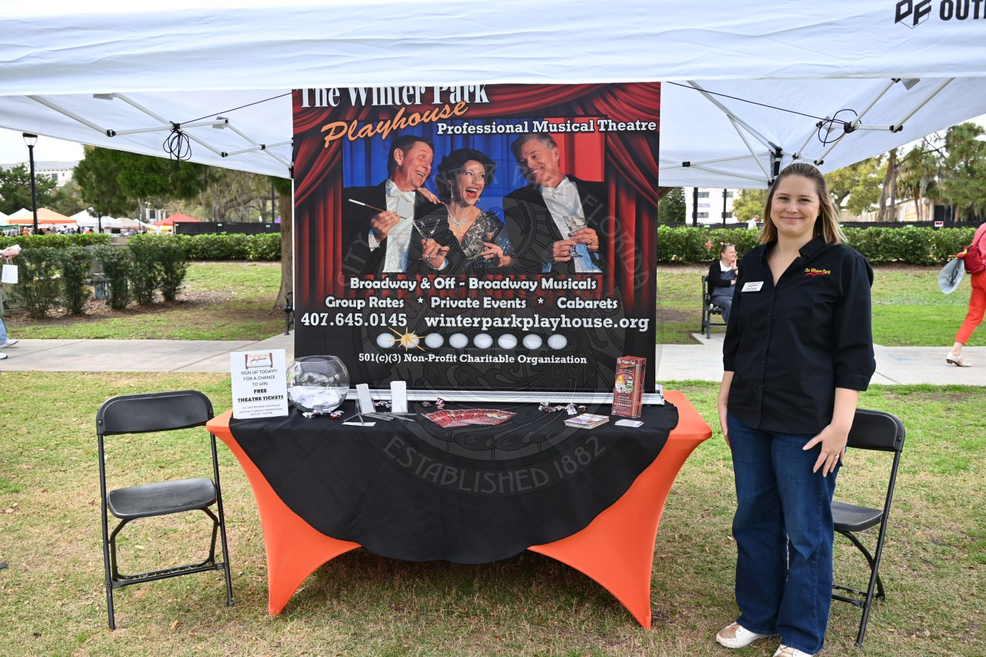a woman standing next to a table that is advertising the winter park playhouse