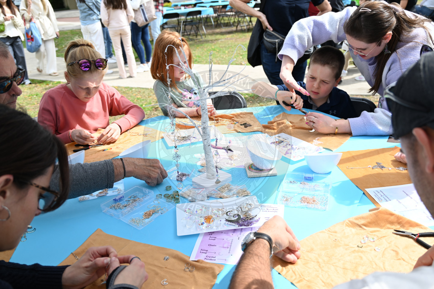 kids sitting down at a table making peices of jewlery.