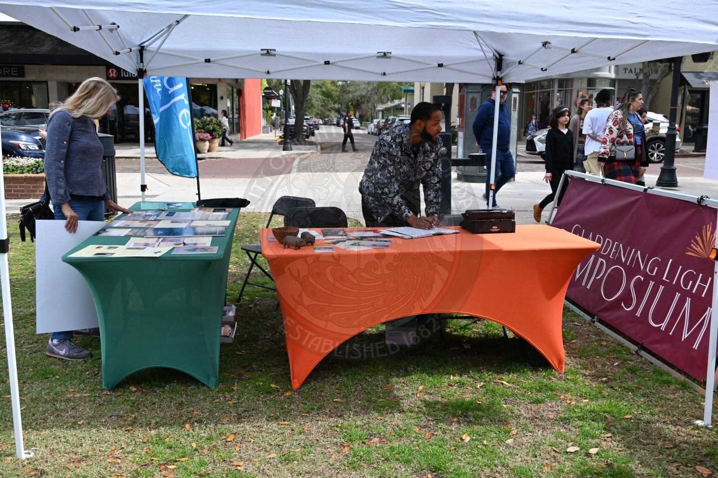 a guy standing behind a table leaning down on the table writing something right next to a typewriter.
