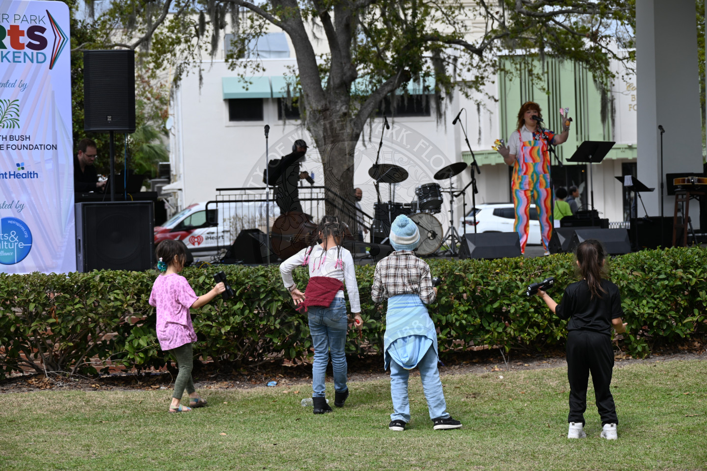 a group of kids standing in front of the stage dancing to a lady performing on the stage with finger puppets.
