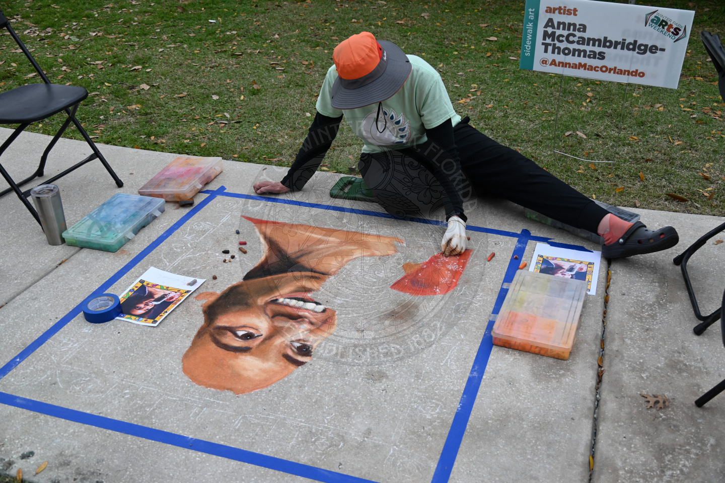 An artist sitting on concrete walkway drawing a person with chalk.