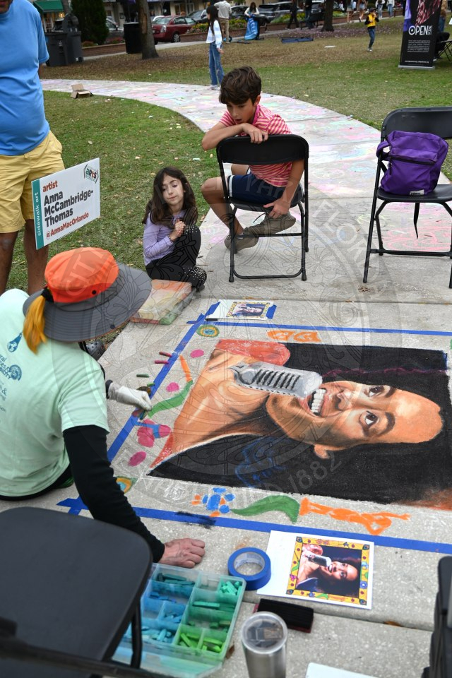 finished sidewalk art with the artist sitting on the alkway and kids looking at the painting in shock