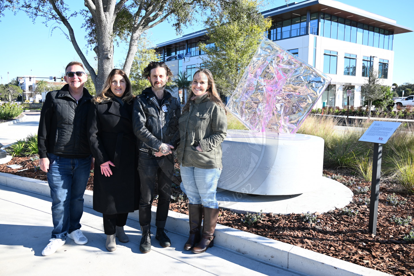 Group of people standing next to each other in front of the glass abstract sculpture.