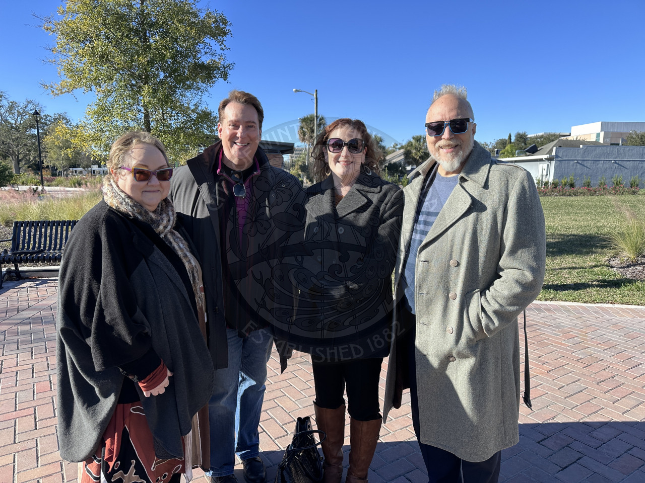 Group of people standing close together in a park smiling.