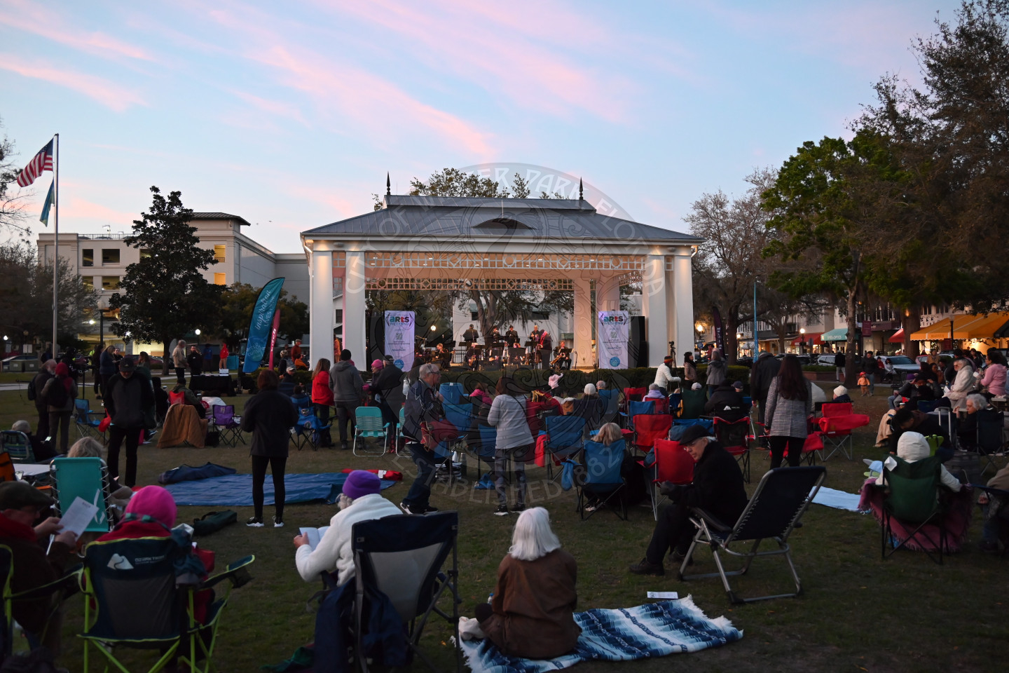 a bunch of people sitting on the grass and in lawn chairs in front of a stage listening to the orchestra perform.