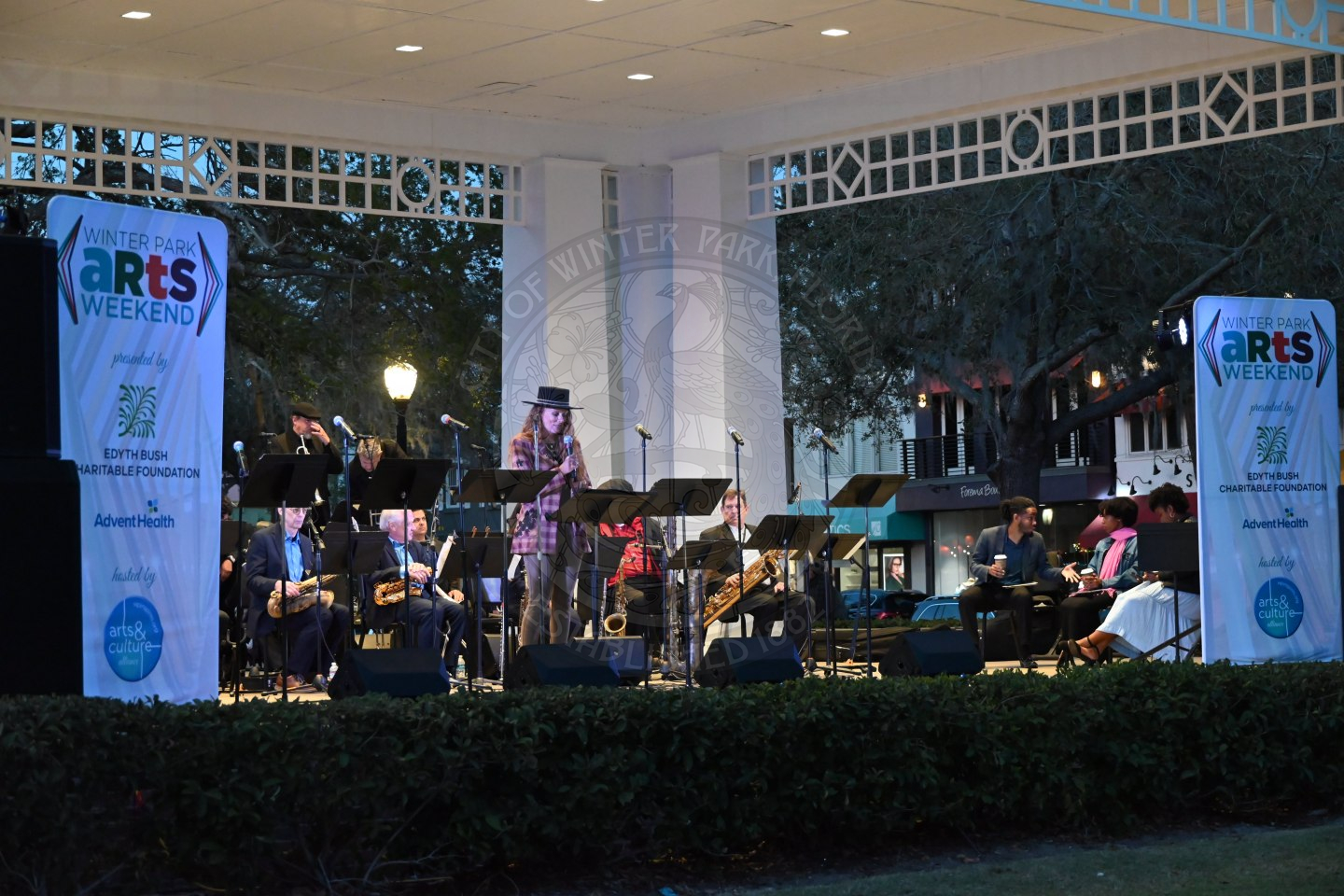 a woman standing on the stage in front of the orchestra talking into a microphone.