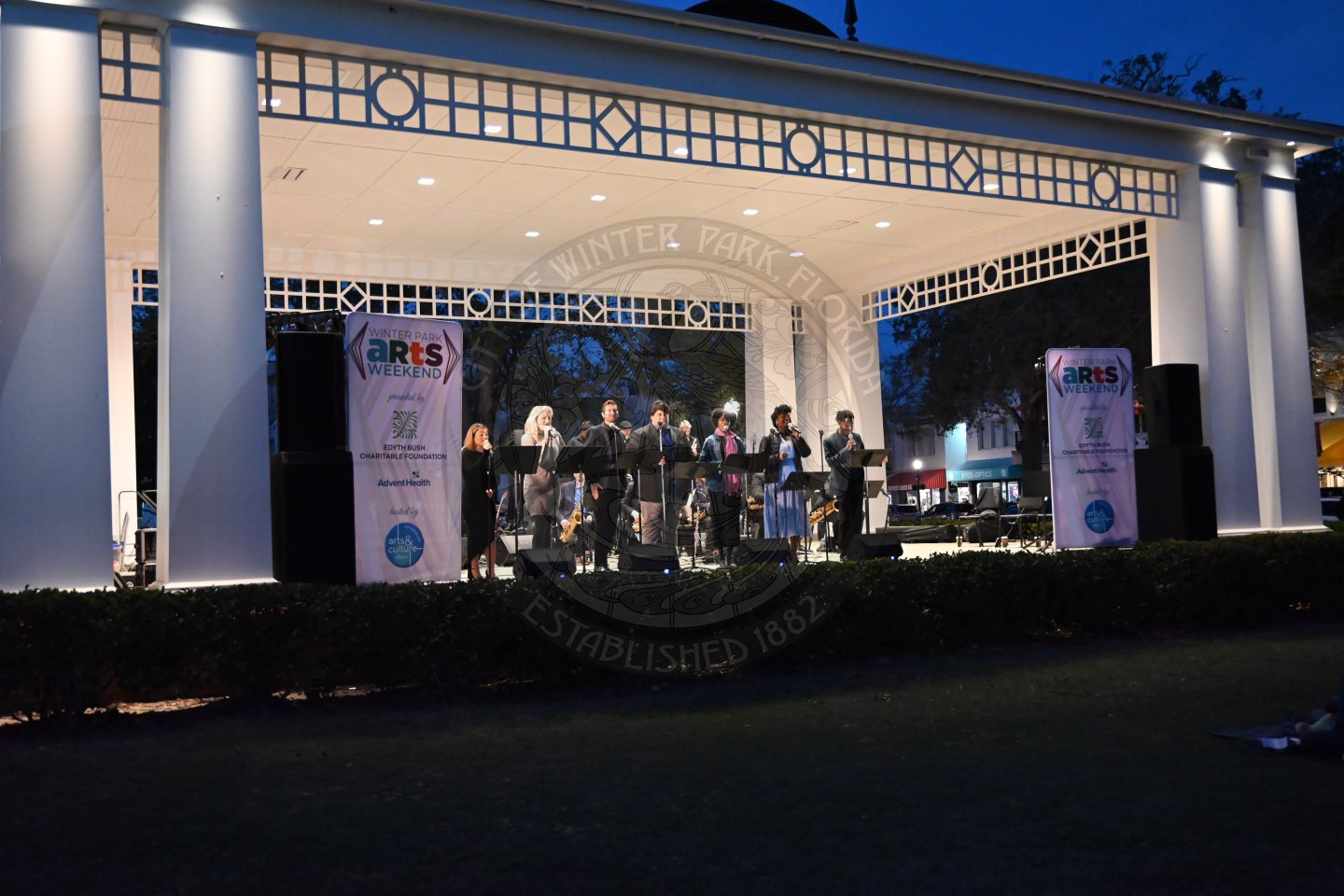 seven singers lined up at the front of the stage with a microphone in front of them singing.