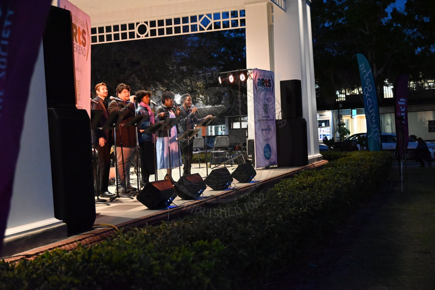 seven singers lined up at the front of the stage with a microphone in front of them singing.