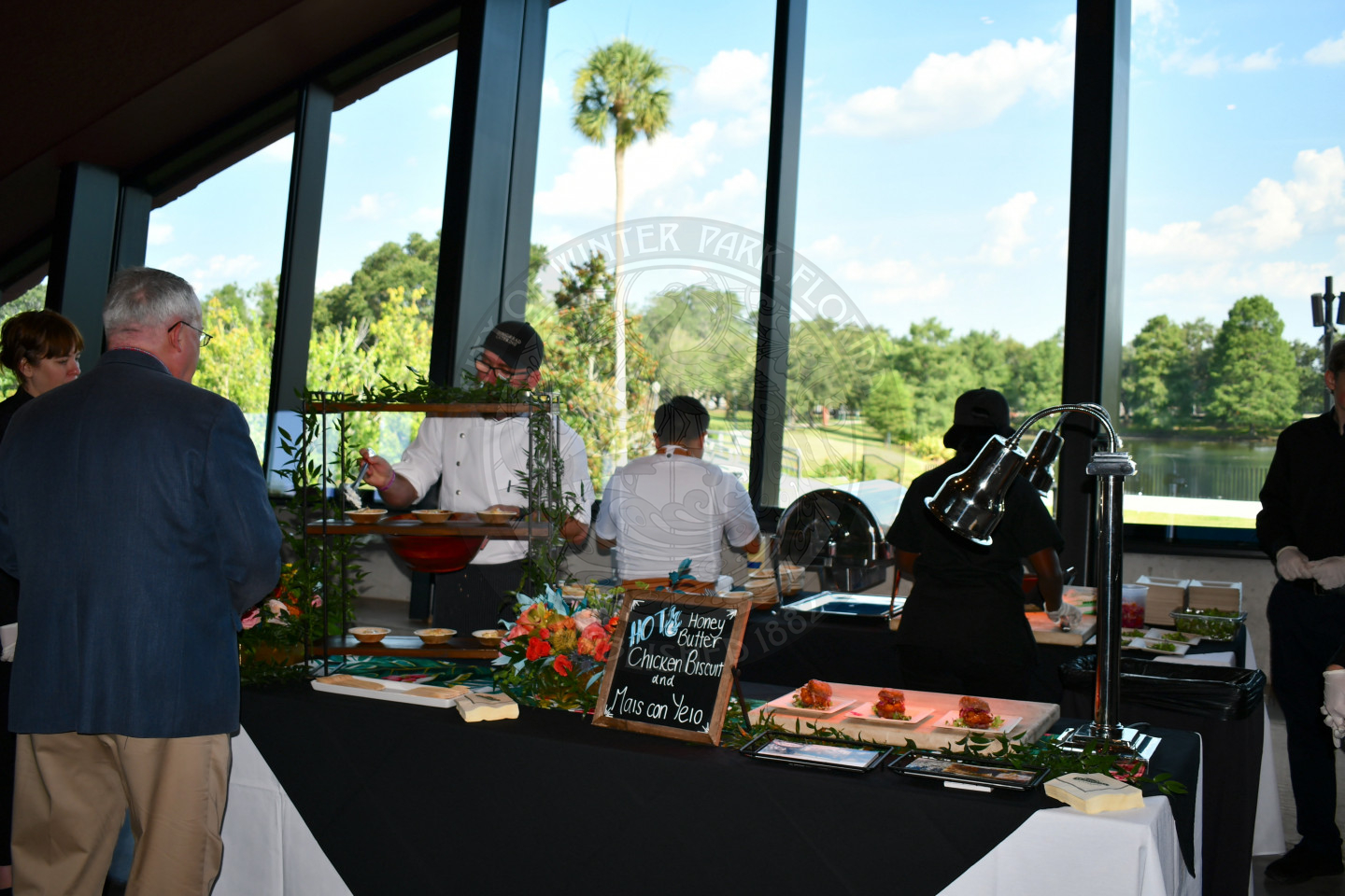 Caterer's behind a table with food displayed.