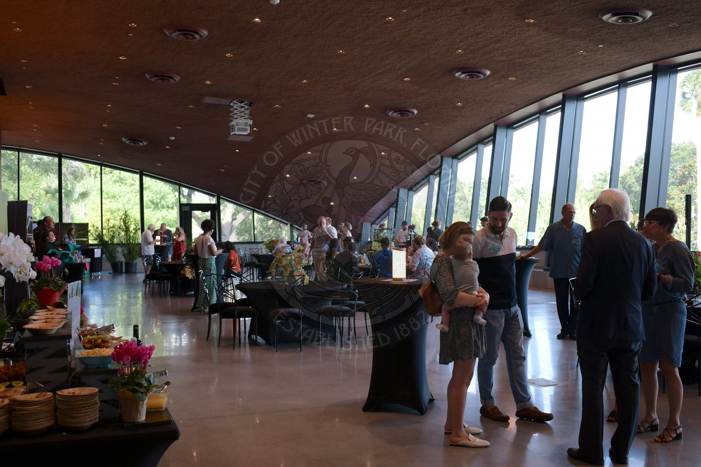 People standing and sitting in a ballroom while drinking and eating food