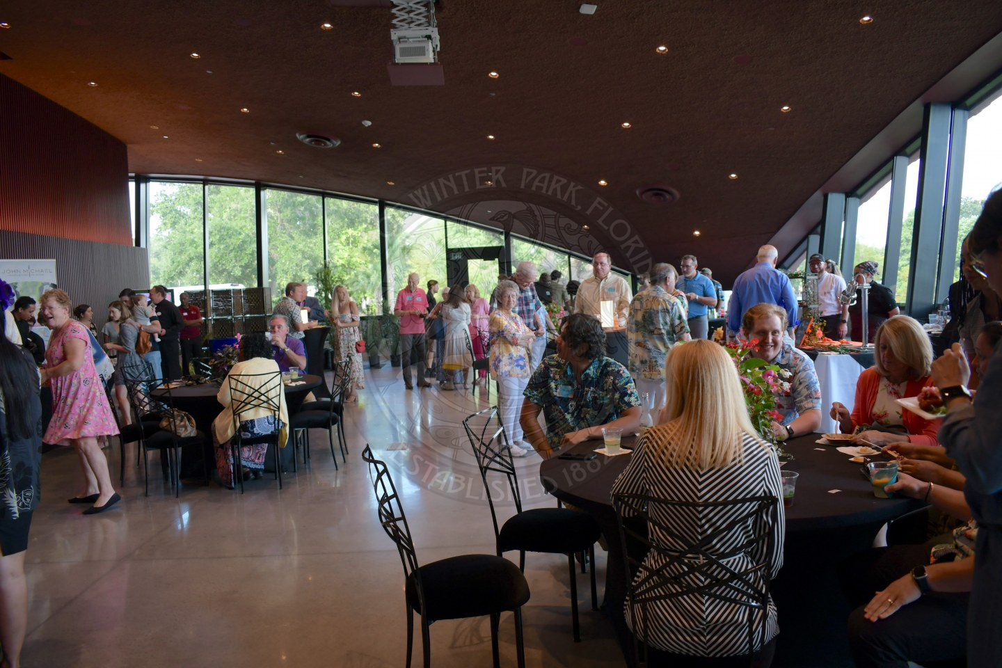 People standing and sitting in a ballroom while drinking and eating food