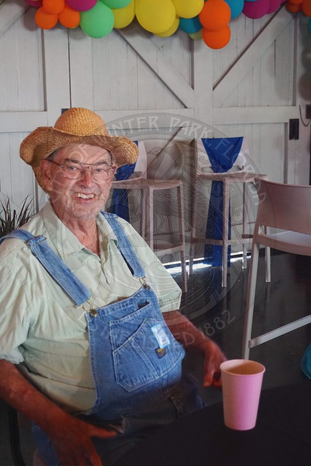 man sitting down wearing overalls and a cowboy hat smiling