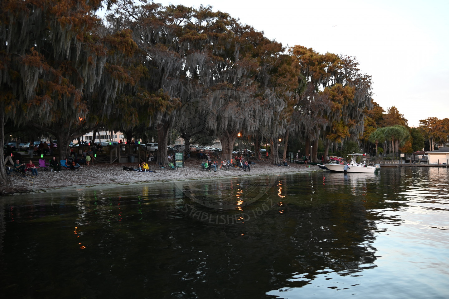 lake shore with people sitting in chairs on the sand to watch the Holiday boat parade
