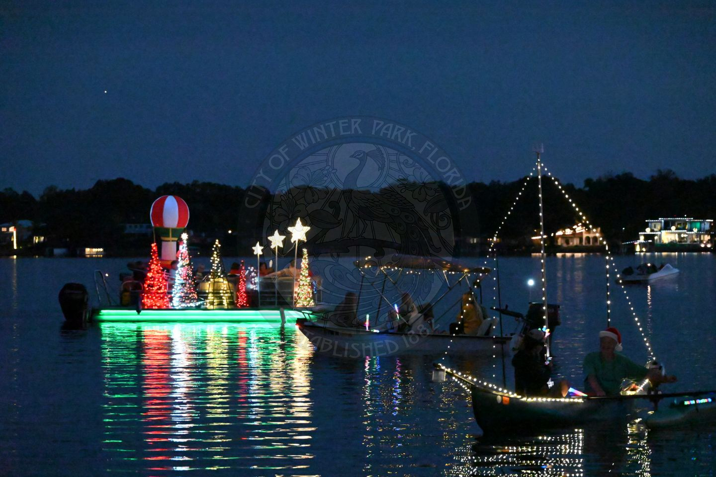 Three tinier boats cruising at night, decorated with holiday lights.