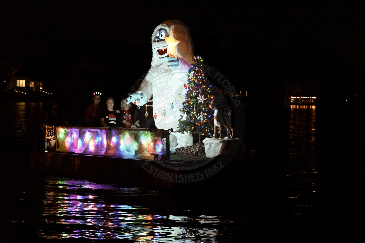 A boat cruising at night, brightly decorated with colorful holiday lights and a huge abominable snowman.