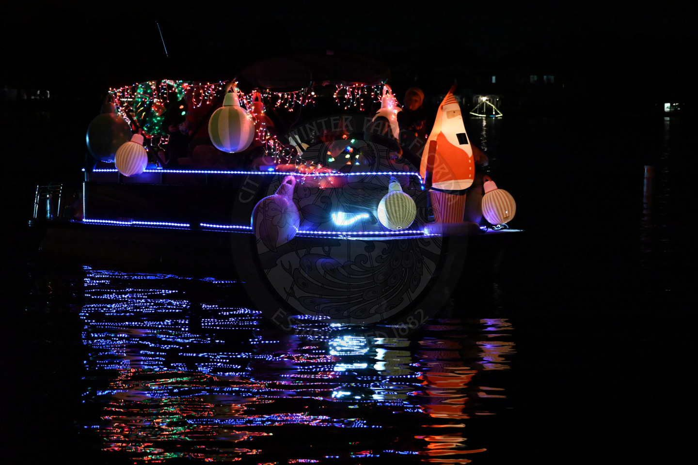A boat cruising at night, brightly decorated with colorful holiday lights and a blow up santa.