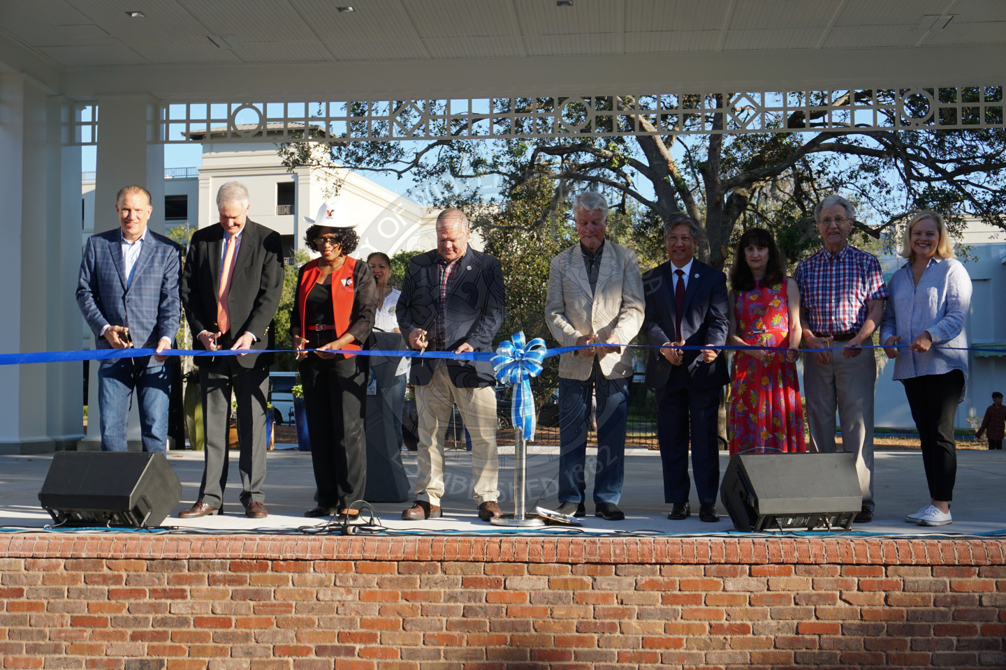 Group of 9 people standing behind a ribbon about to cut it