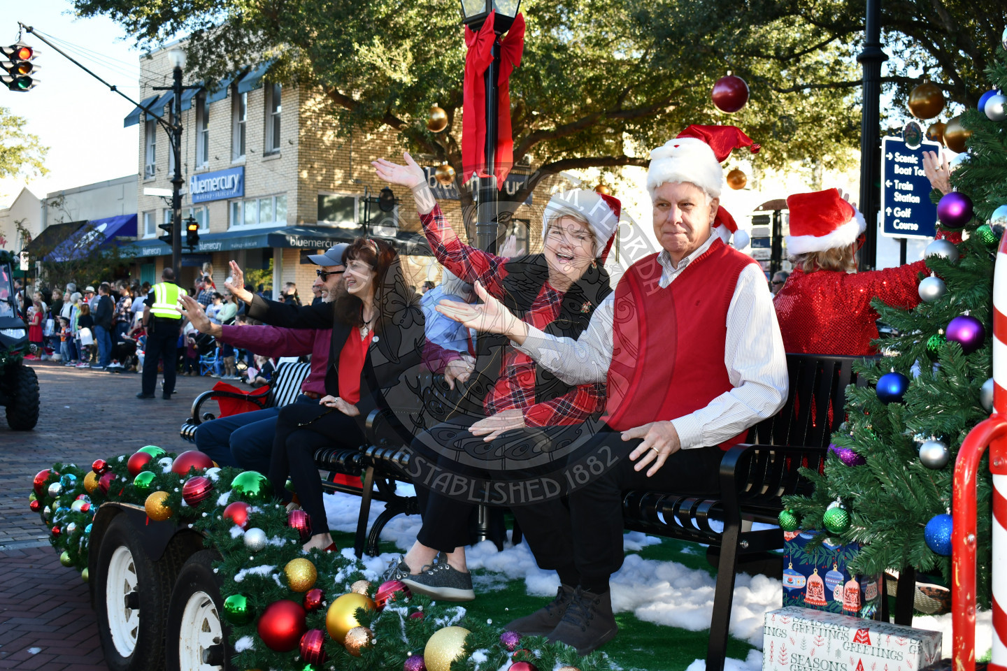two men and women sitting on benches waving to the crowd
